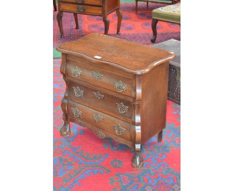 A reproduction oak bombe commode, of small proportions, slightly oversailing top, moulded edge, three drawers, brass loop han