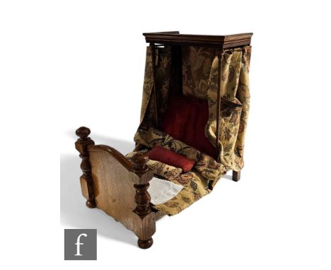 A late 19th or early 20th Century oak doll's half tester bed, moulded edge canopy and turned finial and shaped end, tapestry 