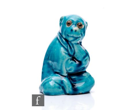 A late 19th Century Arts &amp; Crafts ceramic figure of a seated monkey in robes, in the manner of Burmantofts, having glass 
