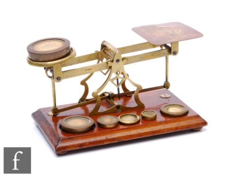 A set of Edwardian brass postal scales with associated weights, on mahogany plinth base, width 28cm. 