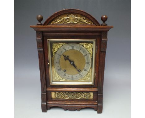 AN EARLY 20TH CENTURY OAK CASED SMALL BRACKET CLOCK, the arched case with ornate brass mounts, the square dial with Roman num
