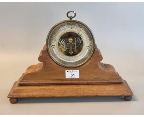 Aneroid hanging brass barometer with silvered face and glass thermometer on a shaped and moulded wooden stand. 35cm wide appr