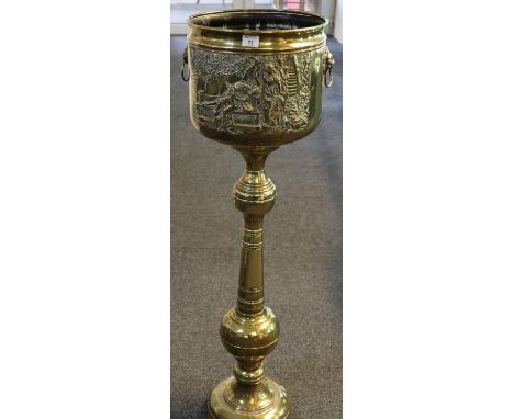 Early 20th century brass repousse jardiniere on stand, decorated with figures within a landscape having lion mask mounts and 