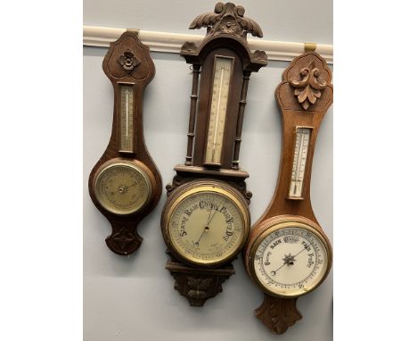 An oak aneroid barometer with a carved top, mercury thermometer and pottery dial together with two other oak aneroid baromete