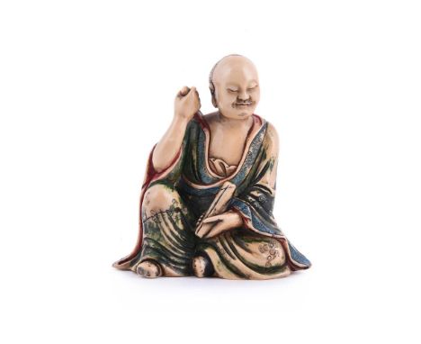 A Chinese soapstone figure of a luohan, the figure shown casually seated and holding a scroll in his left hand, dressed in lo