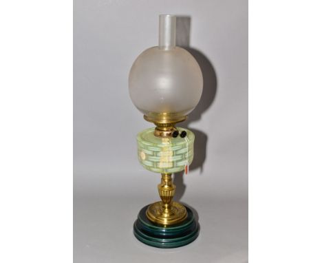 A TWIN BURNER OIL LAMP, having vaseline glass reservoir in basket weave pattern, the brass mount standing on a green ceramic 