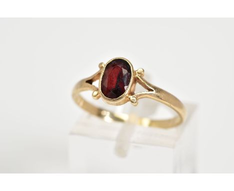 A 9CT GOLD GARNET RING, set with a central oval cut garnet to the bifurcated shoulders and plain polished band, with a 9ct ha