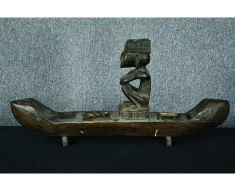 A large carved wooden canoe with a serene looking seated figure. H.39 W.80 cm. 