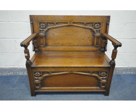 A 20TH CENTURY OAK MONKS BENCH, having a hinged lid and storage compartment, and a carved Gothic front panel, width 107cm x d