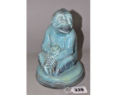 A BESWICK MONKEY FIGURE, number 397, seated on a circular pottery base, holding a piece of fruit, pale turquoise/grey blue gl