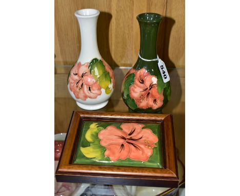 THREE PIECES OF MOORCROFT POTTERY, comprising two coral hibiscus bud vases, one having a cream ground, the other green, heigh