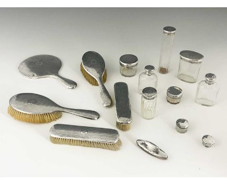 A George V silver eleven-piece dressing table set, comprising hand mirror, four brushes and six glass jars/bottles with silve