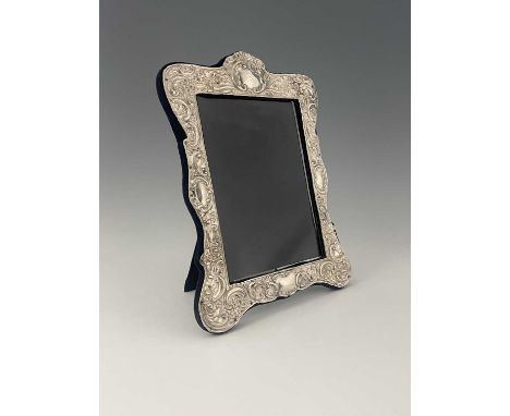 An Edwardian silver mounted photograph frame, of shaped rectangular outline, the silver with four vacant cartouche and decora