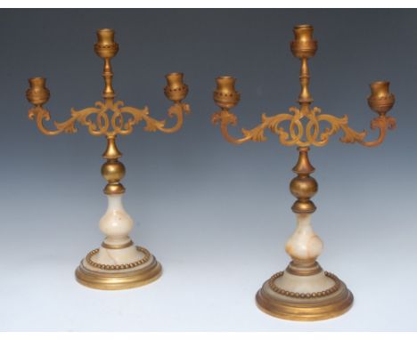 A pair of Gothic Revival gilt metal and alabaster three-light candelabra, pierced and engraved leafy scroll branches, baluste