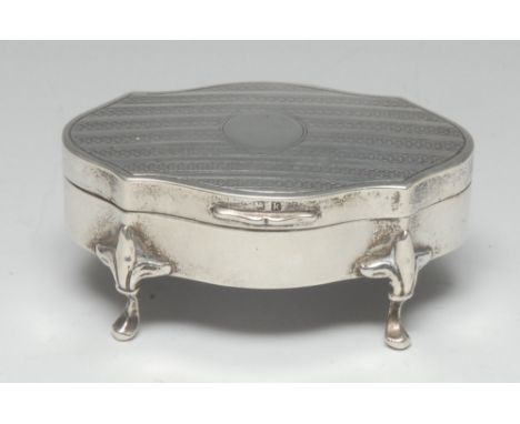 An Edwardian silver shaped oval dressing table trinket box, hinged engine turned cover centred by a vacant circular cartouche