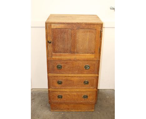 A 1930's light oak side cabinet, enclosed by a single panelled door with three drawers below, fitted brass ring drop handles,