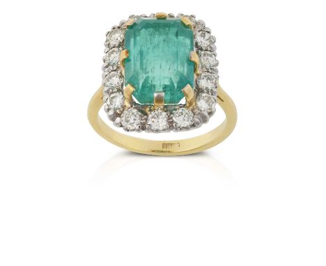 the emerald-cut emerald in a yellow claw setting, within a border of round brilliant cut diamonds in white claw settings, to 