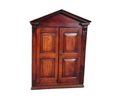 A STAINED WOOD HANGING CORNER CUPBOARD 18th century, with architectural pediment over panelled doors, opening to a shelved in