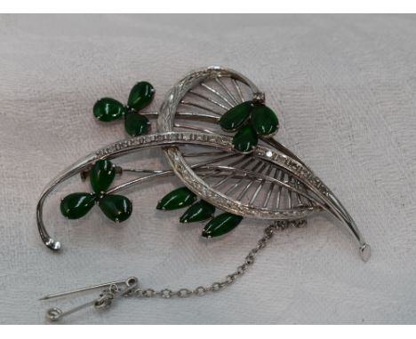 A white metal brooch stamped 18K modelled as a stylised sprig of flowers having diamond and emerald/jade cabouchon decoration