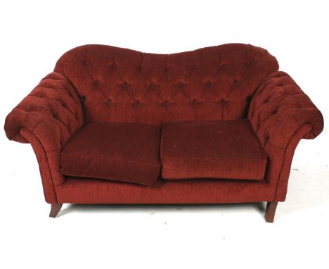 A contemporary two seater button back sofa. Upholstered in red fabric, raised on tapered supports, on casters, H88cm W174cm x