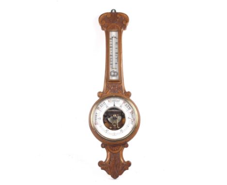 A circa 1900 banjo barometer. With a mercury thermometer positioned over a ceramic dial, the wooden case carved with floral d