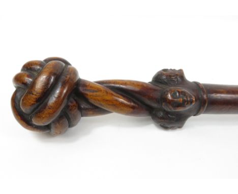 An interesting hardwood club/stick, the top carved with four male heads, 91cm long