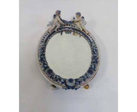 An early 20th Century Meissen style easel back mirror, decorated with two cherubs holding a row of flowers, with a flower enc