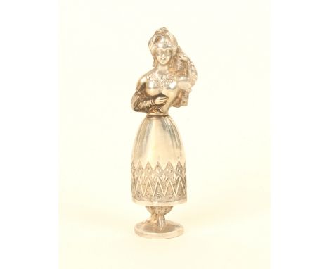 A continental figural silver needlecase in the form of a woman in traditional costume, one hand held to her scarf, the other 