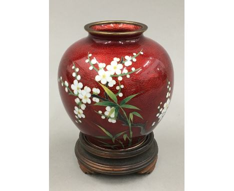 An Oriental ruby ground cloisonne vase decorated with white flowers on a wooden stand