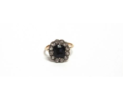 AN EARLY 20TH CENTURY GOLD AND SAPPHIRE OBLONG CLUSTER RING centred with a cushion-shaped dark-blue sapphire, within a near-c
