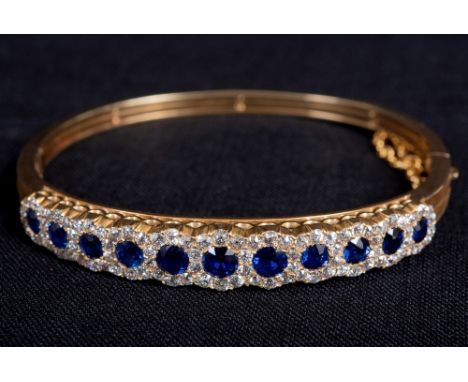 AN EDWARDIAN GOLD, SAPPHIRE AND DIAMOND HINGED BANGLE the front designed as a row of eleven graduated round and slightly cush