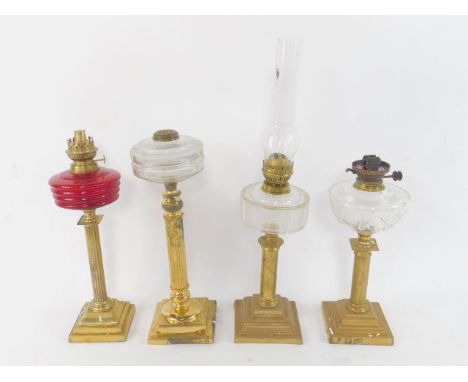 Four brass column oil lamps, one with a fluted ruby glass reservoir, three with faceted clear glass reservoirs, one with chim