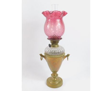A brass twin handled oil lamp, engraved with convolvulous, faceted clear glass reservoir, glass chimney and cranberry glass s