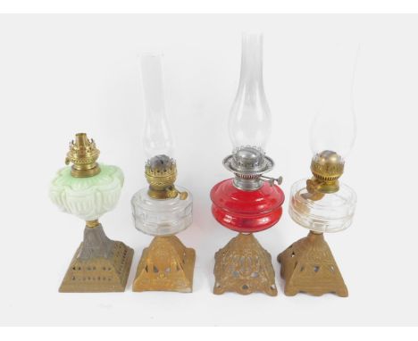 Four Victorian gilt painted cast iron oil lamps, two with faceted clear glass reservoirs, one with a white to green opaline g