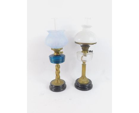A duplex brass oil lamp, with a wrythe and fluted column, raised on a black circular pottery socle, with a fluted blue glass 