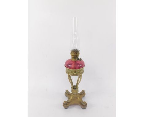 A late Victorian brass oil lamp, with embossed decoration, raised on four fluted supports above a quatrefoil base with a cran