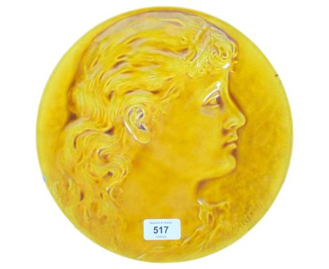 A Burmantofts faience yellow glazed wall-hanging plate, depicting a facial portrait, signed P. Mallet, stamped to reverse, di