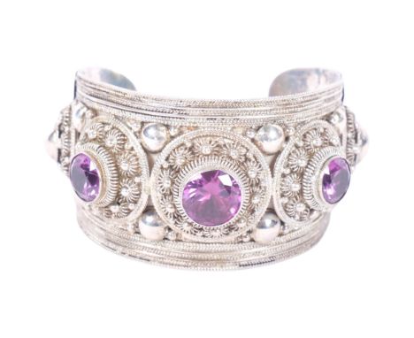 An ornate Siam sterling silver cuff bangle, floral engraved decoration, with raised bosses with amethyst coloured mounts 