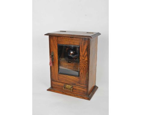 A small oak smoker's cabinet, with a glazed panelled door above a single drawer, enclosing a divisional interior and a lidded