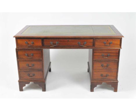 A reproduction mahogany pedestal desk, with a tooled inset green leather top, above a sliding central drawer flanked by banks