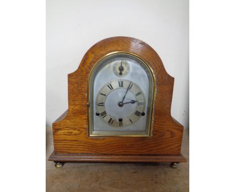 An Edwardian oak cased mantel clock with silvered dial on raised brass feet  CONDITION REPORT: With pendulum but no key. 