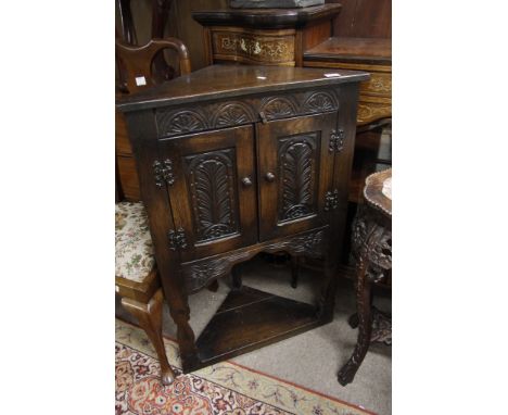 A carved oak corner cupboard fitted with an under shelf 
