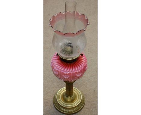 A late Victorian oil lamp with a brass column and pink glass with a shade and chimney 