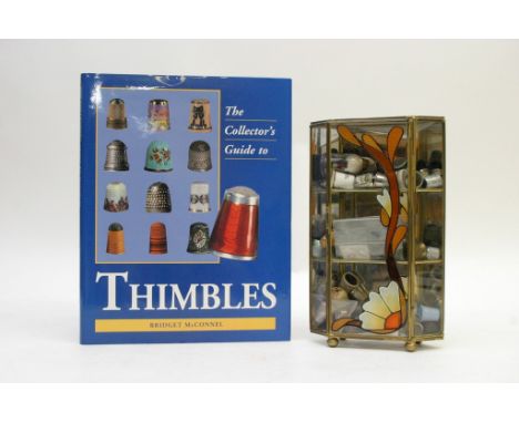 A small display case containing an assortment of thimbles together with a book, The Collector's Guide to Thimbles by Bridget 