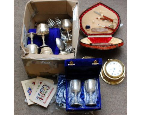 A box containing silver plated cutlery, a brass clock and compass, cased manicure set and silk postcards