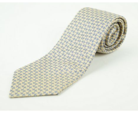 An Hermes silk tieWith a blue woven 'H' repeating pattern, to a pale ochre ground, length 152cm