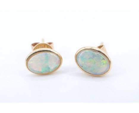 A modern pair of opal ear studs, having 7 x 6 mm oval opals bezel set on a yellow metal (tests as high carat gold) butterfly 