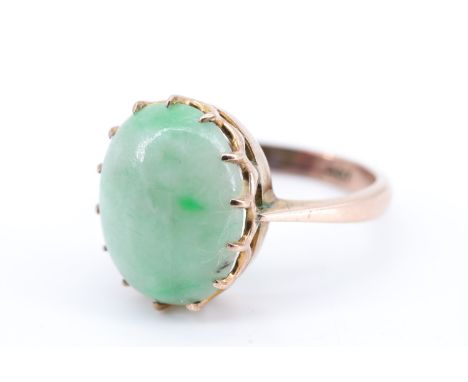 An early 20th Century lady's jade finger ring, having a oval jade cabochon (11 x 13 mm) set on a gallery between tapering sho