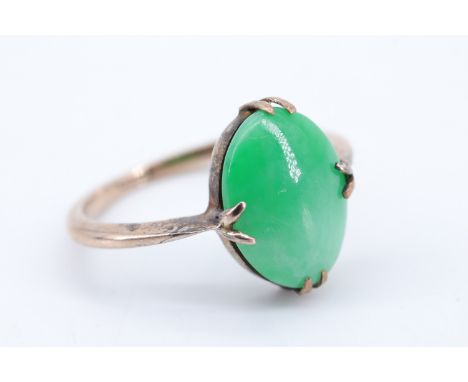 An early 20th Century jade and yellow metal ring, the oval jade cabochon (11 x 9 mm) held by four bifurcated prongs on a plai