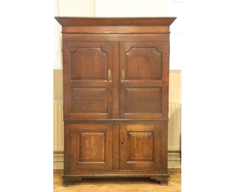 An early 19th Century joined oak press cupboard, having an angular cornice above a pair of fielded-panelled doors enclosing a